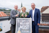 Landesrat Max Hiegelsberger, Edeltraud Huemer und Gerald Hackl stehen nebeneinander auf einer Dachterrasse, jeder hält ein schönes Glas mit Most in der Hand, davor eine Schild mit Beschriftung Wild auf Most