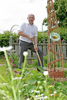 Landesrat Max Hiegelsberger in einem Garten mit einem Spaten, neben ihm ein Gestaltungselement aus Zweigen mit einer Natur im Garten-Plakette