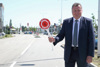 Landesrat Mag. Günther Steinkellner steht am Rand einer Straße und hält eine Kelle mit Beschriftung Halt Polizei in der Hand