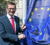Landesrat Achleitner steht neben einem Fahnenmast und hält die daran befestigte Europa-Fahne