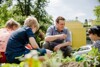 Landesrat Stefan Kaineder hockt mit Kindern in einem Acker und hält eine Pflanze in der Hand.
