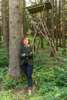 Landesrätin Michaela Langer-Weninger steht in einem Wald an einen Baumstamm gelehnt, auf dem ein Fragezeichen aufgesprüht ist, dahinter ein Jägerstand aus Holz
