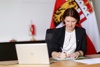 Landesrätin Michaela Langer-Weninger sitzt an einem Schreibtisch, vor ihr ein Laptop, im Hintergrund Oberösterreich-Fahne