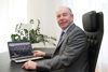 Landtagspräsident Max Hiegelsberger sitzt an einem Tisch, vor ihm ein Laptop, auf dessen Bildschirm die neue Homepage des Oö. Landtags zu sehen ist