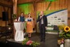 Stephan Eichelsberger, Theresa Neubauer und Landesrat Max Hiegelsberger mit Mikrophon stehen auf einer mit Blumen geschmückten Bühne