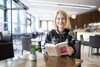 Landeshauptmann-Stellvertreterin Mag.a Christine Haberlander sitzt an einem Tisch in einem Café und hält ein Buch in Händen