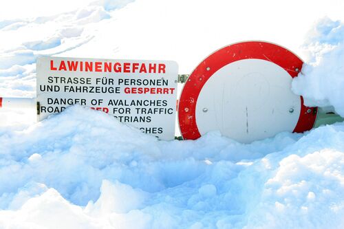 Verkehrsschild Einfahrt verboten und Schild mit Aufschrift `Lawinengefahr Straße für Personen und Fahrzeuge gesperrt` stecken im Schnee