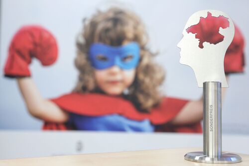 Ein wie ein Superheld bekleidetes Mädchen mit roten Boxhandschuhen schaut auf den Sonderpreis,  der vor ihr steht und einen Kopf mit  oberösterreichischer Landkarte darin zeigt