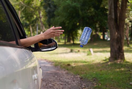 Nahaufnahme eines Autos, jemand wirft eine Plastikflasche aus dem offenen Fenster. 