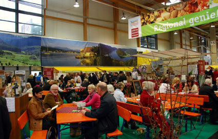 Messebesucherinnen und - besucher an Tischen in der Messehalle Ried