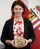Agrar-Landesrätin Michaela Langer-Weninger mit einem Laib Brot in den Händen, im Hintergrund die Oberösterreich-Fahne.