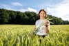 Agrar-Landesrätin Mag.a Michaela Langer-Weninger steht in einem Kornfeld und hält drei Ähren in der Hand, am Ende des Feldes befindet sich eine Laubbaumreihe.