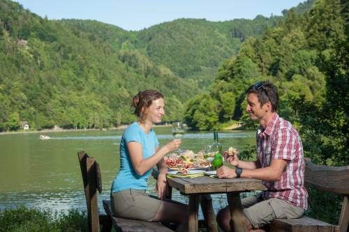 Frau und Mann trinken und essen an einem Tisch am Ufer der Donau