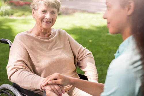 Dunkelhäutige Pflegerin und Seniorin im Rollstuhl