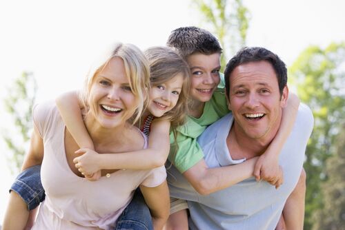 Eine junge Frau und ein junger Mann stehen nebeneinander und schultern jeweils ein Mädchen und einen Jungen. 