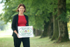 Landesrätin Michaela Langer-Weninger steht in einem Park mit großen Bäumen, sie hält ein Schild in Händen mit Beschriftung Natur im Garten