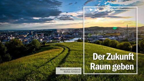 Blick vom Pfenningberg mit grüner Wiese im Vordergrund auf Linz mit der Aufschrift:  Der Zukunft Raum geben – Wirtschafts-Landesrat Markus Achleitner