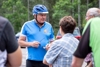 Landesrat Mag. Günther Steinkellner im Rad-Dress mit Helm im Gespräch mit zwei weiteren Personen, im Hintergrund Wald und parkende Autos