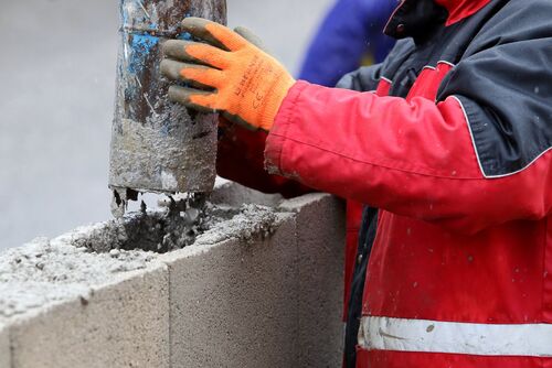 Arbeiter gießt flüssigen Beton in einen Betonziegel auf einer Mauer aus Betonziegeln