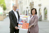 Mag. Dietmar Krenmayr und Landesrätin Birgit Gerstorfer stehen auf einem Stadtplatz und halten gemeinsam ein Poster mit einem Foto mit lachender Jugendlicher und der Beschriftung Young @ clever sowie Informationen zu Ausgehzeiten, Alkohol und Nikotin