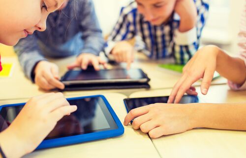 Jugendliche sitzen bei einem Tisch und bedienen Tablets