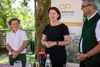 Ingrid Schmaranzer (Österreichischer Erwerbsimkerbund), Agrar-Landesrätin Michaela Langer-Weninger und OÖ LK-Präsident Franz Waldenberger stehen nebeneinander in einem Garten; vor ihnen sind auf einem Tisch ein Mikrofon und mehrere Trinkflaschen zu sehen.