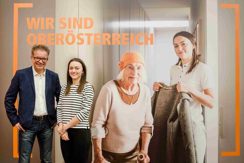 Landesrat Rudi Anschober und Oksana Protsiv vor einem Plakat zum Thema Pflege mit der Aufschrift Wir sind Oberösterreich