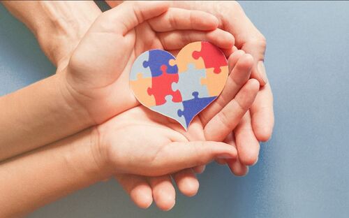 Herz aus Puzzleteilen liegt in Kinderhänden, die von beiden Hände eines Erwachsenen gehalten werden