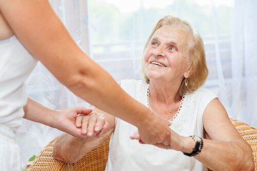 Pflegerin reicht einer älteren Frau die Hände 