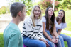 Vier junge Menschen im gemeinsamen Gespräch sitzend in einem Park.