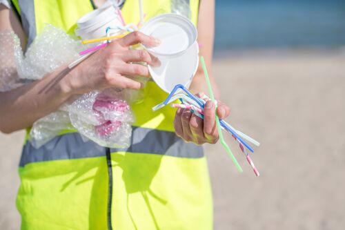 Reinigungskraft trägt Plastikbecher, Strohhalme und anderes Wegwerfplastik.