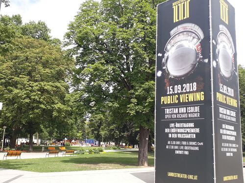 Im Vordergrund des Linzer Volksgartens stehende Säule mit der Ankündigung des Public Viewings von Richard Wagners „Tristan und Isolde“ am 15. September 2018. 