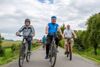 Landesrat Ing. Wolfgang Klinger, Landesrat Mag. Günther Steinkellner und  Landesrat Max Hiegelsberger radeln nebeneinander auf dem Radweg durch eine Landschaft mit Wiesen und Feldern