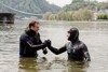 LR Stefan Kaineder und der „schwimmenden Professor“ Prof. Dr. Andreas Fath stehen zur Hälfte in der Donau beim Handshake.  Dahinter befinden sich Gebäude und ein Schiff.