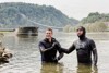 LR Stefan Kaineder und der „schwimmenden Professor“ Prof. Dr. Andreas Fath stehen zur Hälfte in der Donau beim Handshake.  Dahinter befinden sich Gebäude und ein Schiff.