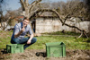 Landesrat Stefan Kaineder in einem Garten mit einem Brocken Erde in der Hand, vor ihm ein Bereich mit Erde und zwei Gemüsekisten