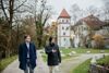 Landesrat Stefan Kaineder und Thomas Rammerstorfer gehen nebeneinander auf einem Weg in einem Park, im Hintergrund ein schlossähnliches Gebäude, das Minoritenkloster Wels