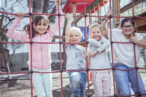 Vier Kinder stehen vor einem Kletternetz, dahinter ein Gebäude.