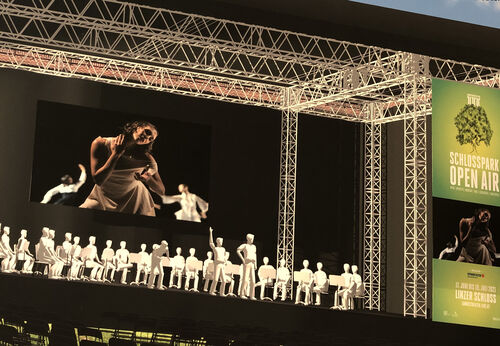 Grafik einer Bühne mit Tänzerin und Orchester, Videowände mit Beschriftung Schlosspark Open Air