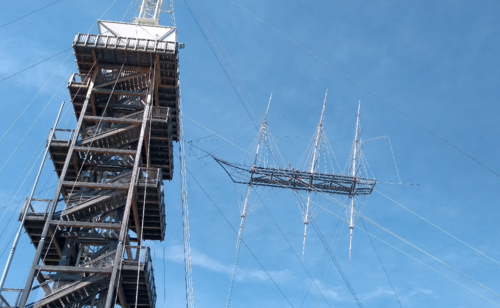 Turm mit Mast und schwebendes Schiff vor blauem Himmel hoch über Linz