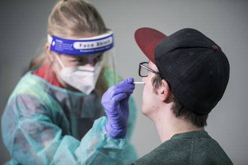 Frau in Schutzkleidung nimmt einem jungen Mann mit einem Teststäbchen eine Probe aus der Nase ab
