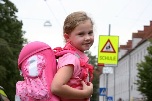 Mädchen mit Schultasche vor dem Hinweisschild Achtung Schule