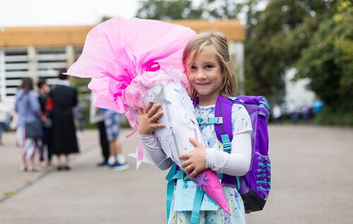 Ein kleines Mädchen freut sich vor dem Schuleingang mit ihrer Tüte auf den ersten Tag in der Schule.