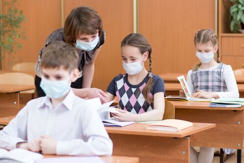 Schülerinnen, Schüler und Lehrerin mit Mund-Nasen-Schutz im Klassenzimmer