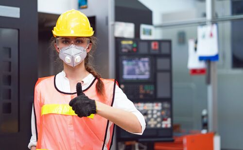 Eine junge Technikerin mit Helm und Maske freut sich über ihren neuen Job.