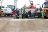 LR Markus Achleitner, LR Mag. Günther Steinkellner und Hörschings Bürgermeister Klaus Wahlmüller stehen nebeneinander hinter einem Hügel mit Sand und jeweils mit einem Spaten in der Hand; hinter ihnen sind mehrere Baufahrzeuge zu sehen