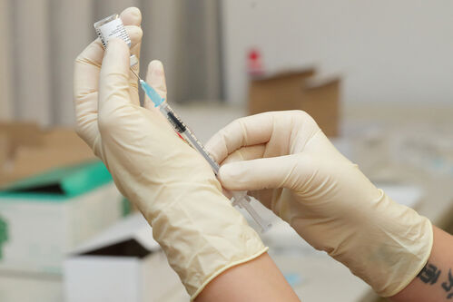 Hände in Schutzhandschuhen, Impfstoff wird aus einer Ampulle in eine Spritze aufgezogen