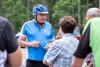 Landesrat Mag. Günther Steinkellner in Rad-Dress und mit Radhelm im Gespräch mit mehreren Personen, im Hintergrund parkende Autos, Wald