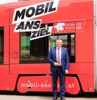 Landesrat Mag. Günther Steinkellner steht vor einer Straßenbahn, diese ist beschriftet mit Mobil ans Ziel, die Mobilitätsinitiative OÖ