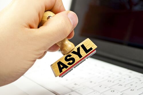 Hand hält Stempel mit der Aufschrift „Asyl“. 